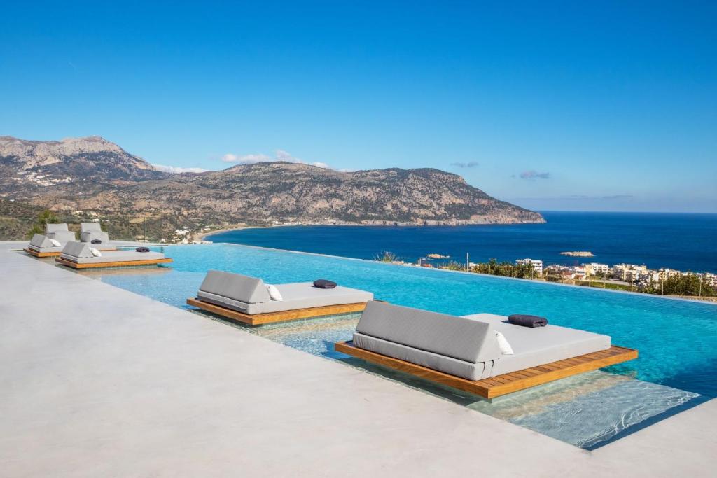 a row of beds on a pool with the ocean at ISTIA LUXURY VILLAS in Karpathos