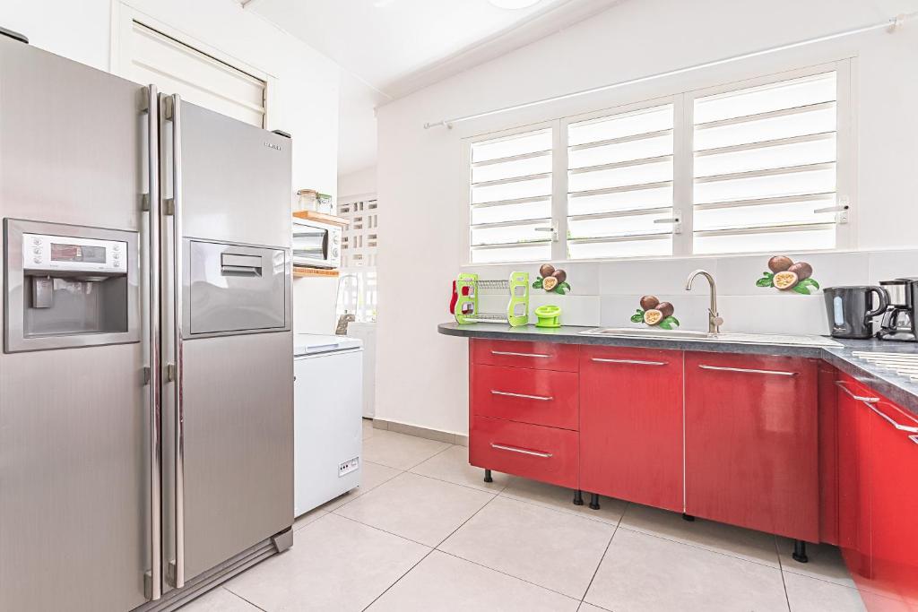 a kitchen with red cabinets and a stainless steel refrigerator at Villa de 3 chambres avec piscine privee jacuzzi et jardin clos a Baie Mahault in Baie-Mahault
