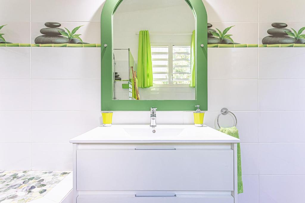 a bathroom with a white sink and a green mirror at Villa de 3 chambres avec piscine privee jacuzzi et jardin clos a Baie Mahault in Baie-Mahault