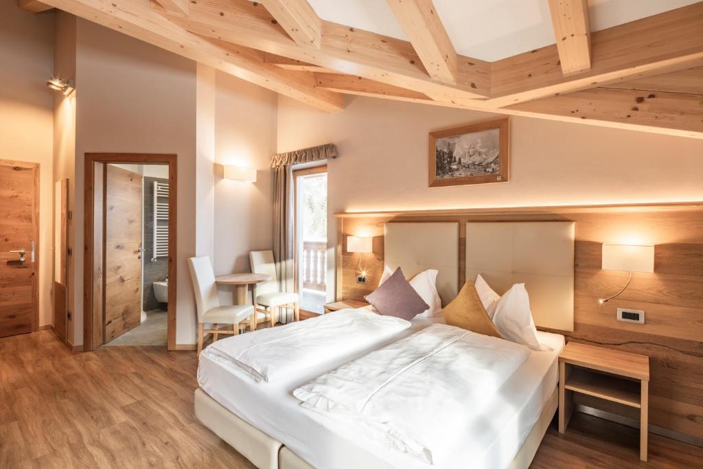 sypialnia z dużym białym łóżkiem i drewnianym sufitem w obiekcie Albergo Belvedere w mieście Vigo di Fassa
