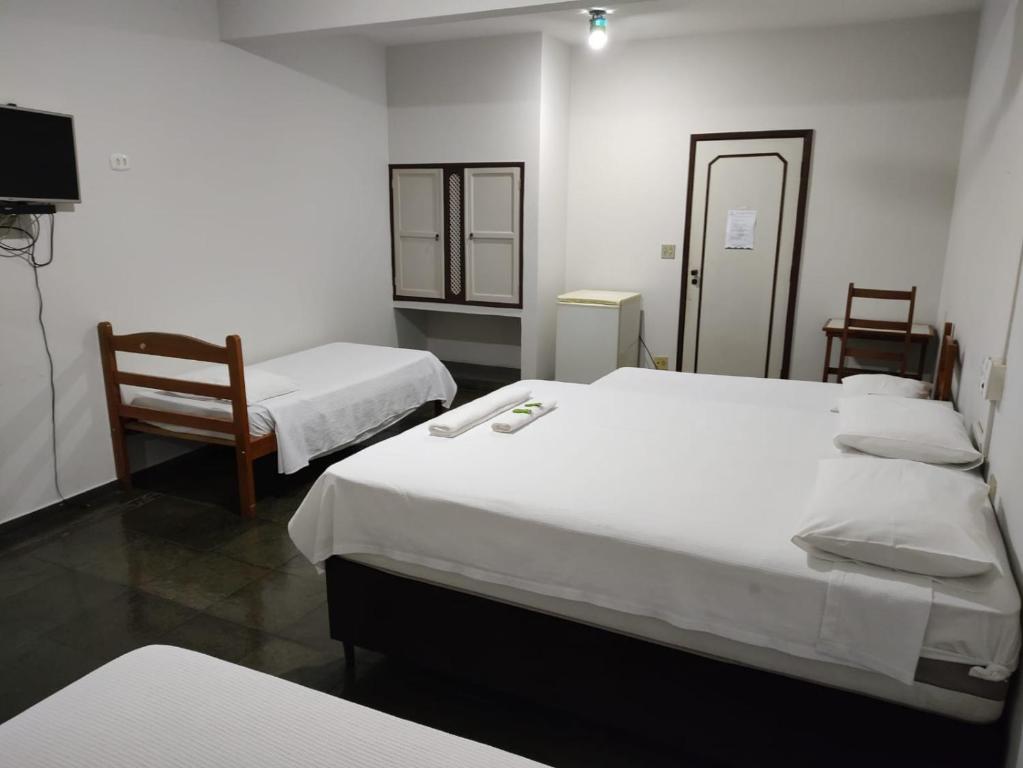 a room with three beds and two chairs and a television at Hotel Village Cataguases in Cataguases