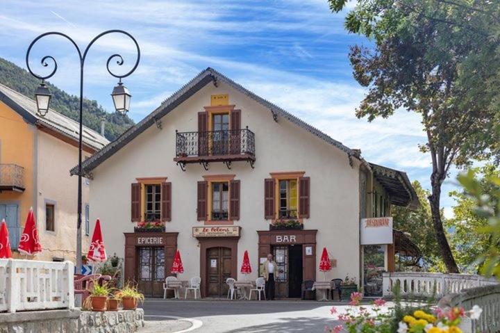 a white building with a balcony and tables and chairs at Gite Le Pelens in Saint-Martin-dʼEntraunes