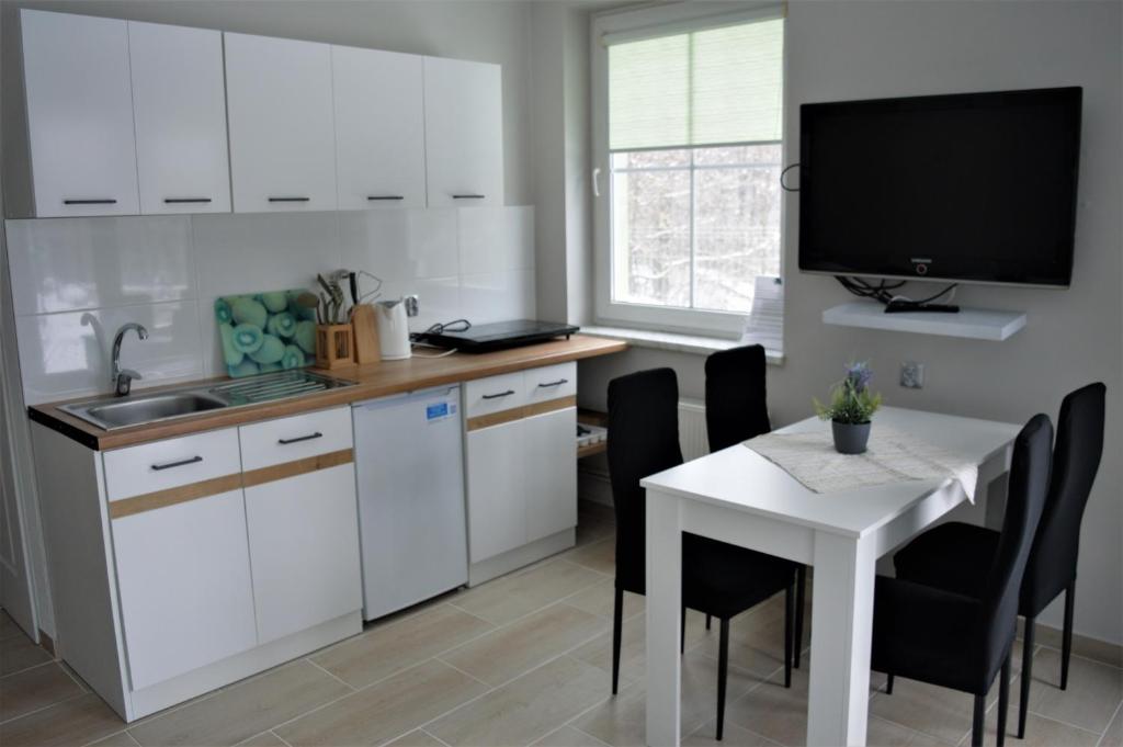 uma cozinha com armários brancos, uma mesa e uma televisão em Zielony Domek em Karpacz