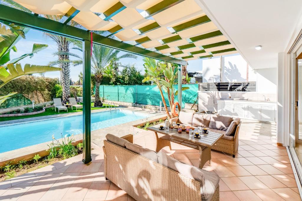 eine Terrasse mit Tisch und Stühlen neben einem Pool in der Unterkunft Villa Poseidon Gardens by Ezoria Villas in Larnaka