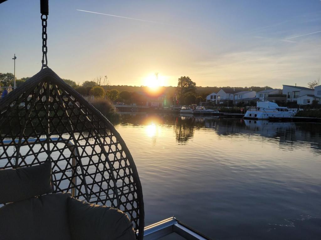 a boat on a river with the sun setting at L&#39;Escale Royale L&#39;Isle Adam à 20 minutes de Paris CDG in LʼIsle-Adam