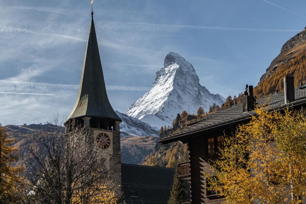 a mountain behind a building and a church with a tower at Matterhorn Lodge Boutique Hotel & Apartments in Zermatt