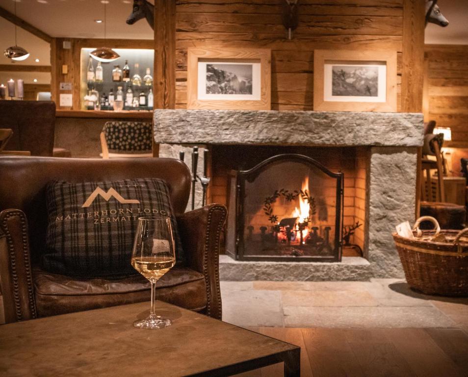 a glass of wine sitting on a table in front of a fireplace at Matterhorn Lodge Boutique Hotel & Apartments in Zermatt