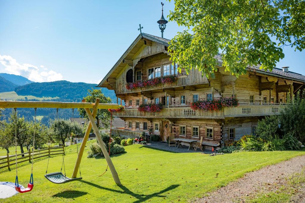 a large wooden house in a field with a swing at Drittlhof in Hopfgarten im Brixental