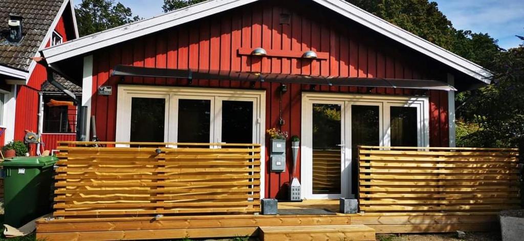 una casa roja con un gran porche de madera en ÖLJERSJÖ COTTAGE en Lyckeby