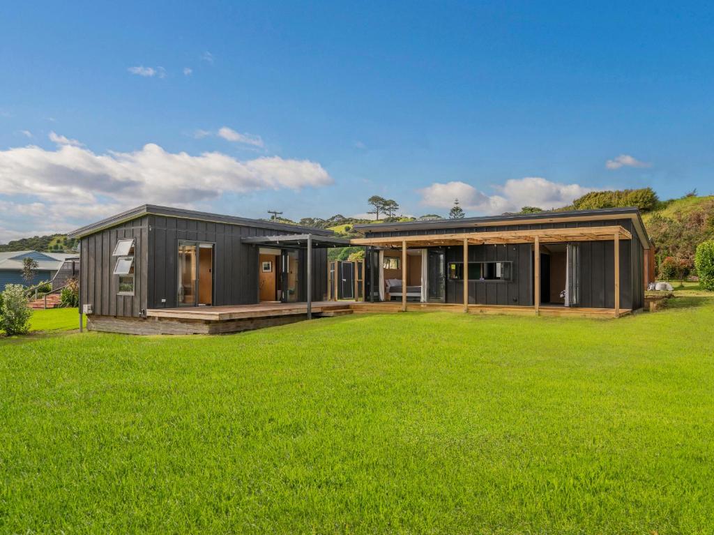 a black house with a large green yard at The Little Bach at Whangapoua in Whangapoua
