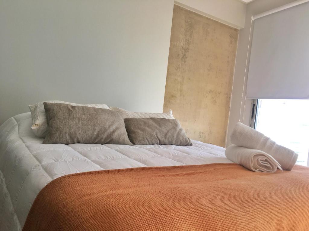 1 cama naranja y blanca con almohadas y ventana en Departamento Minimalista en pleno centro en San Miguel de Tucumán