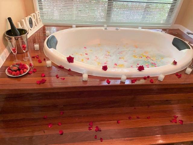 a bath tub filled with red rose petals on a wooden floor at Amore On Buderim Rainforest Cabins in Buderim