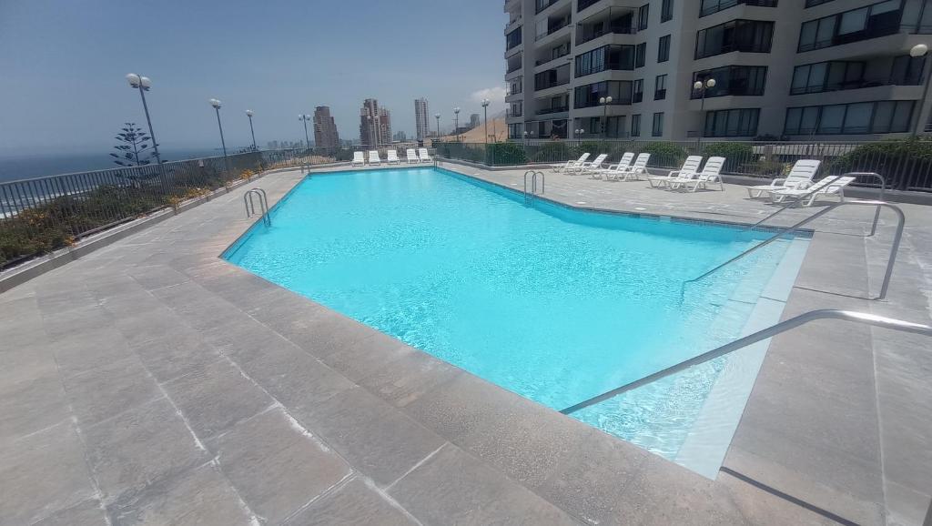 a large swimming pool with chairs and a building at Reservas altos de huayquique in Iquique