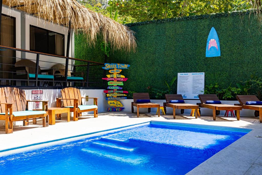 a swimming pool with chairs and a table and a surfboard at Shark Town Mal Pais in Santa Teresa Beach