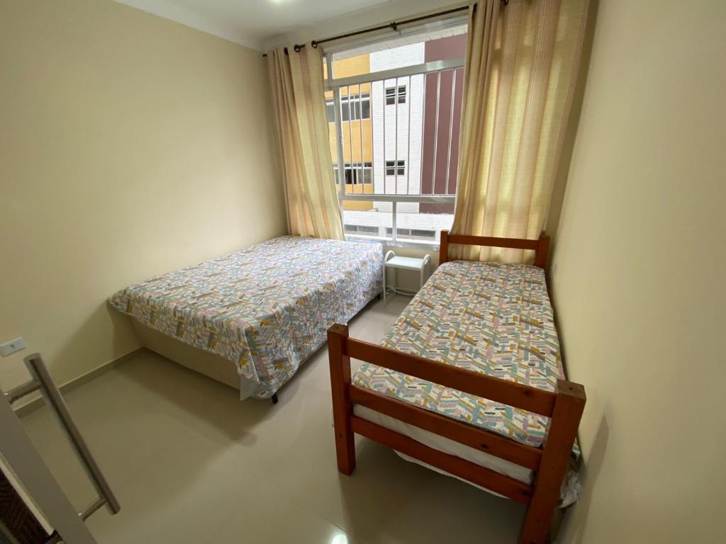 um pequeno quarto com duas camas e uma janela em Apartamento frente mar Gonzaga Santos em Santos