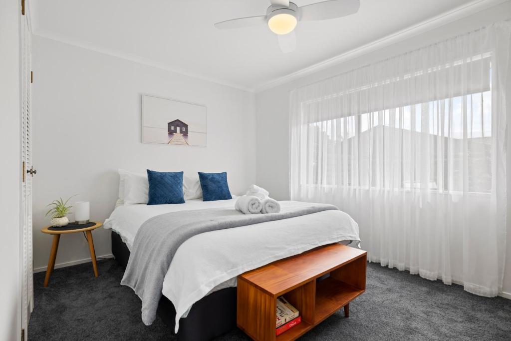 a white bedroom with a large bed with blue pillows at Waitui Wonder - A Comfortable Escape in Mount Maunganui