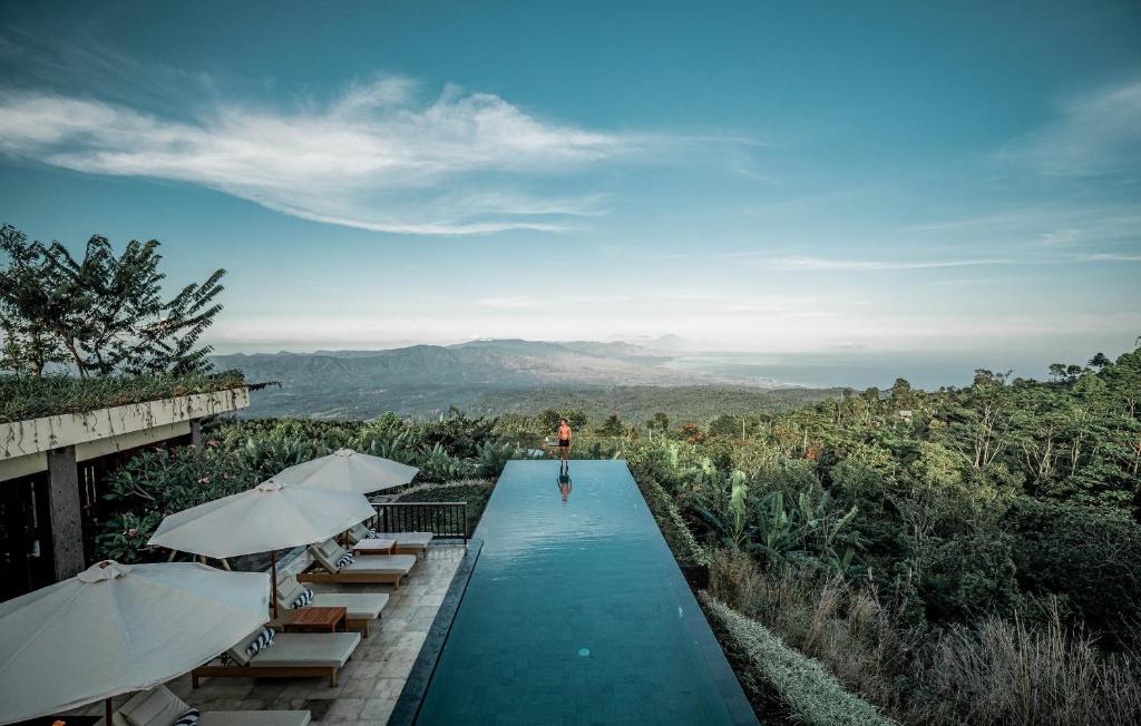 ein Pool mit Tischen und Sonnenschirmen auf einem Hügel in der Unterkunft Munduk Moding Plantation Nature Resort in Munduk