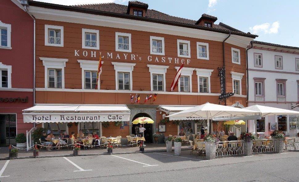 ein Hotel mit Tischen und Sonnenschirmen vor einem Gebäude in der Unterkunft Hotel Gasthof Kohlmayr in Gmünd in Kärnten