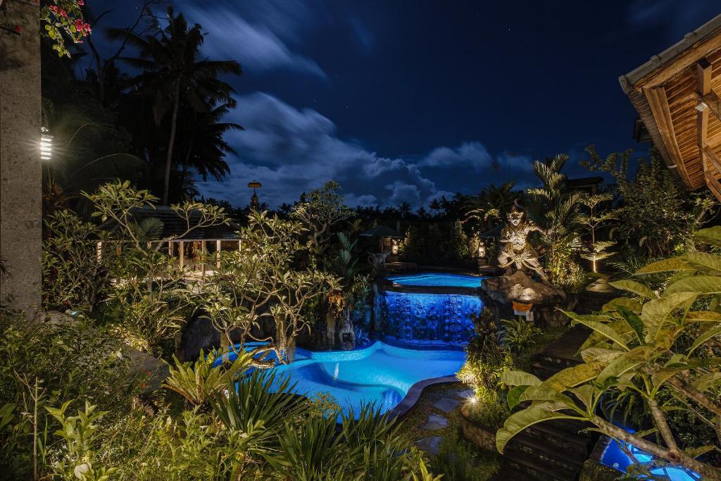 a garden at night with a swimming pool at Gynandha Ubud Cottage in Ubud