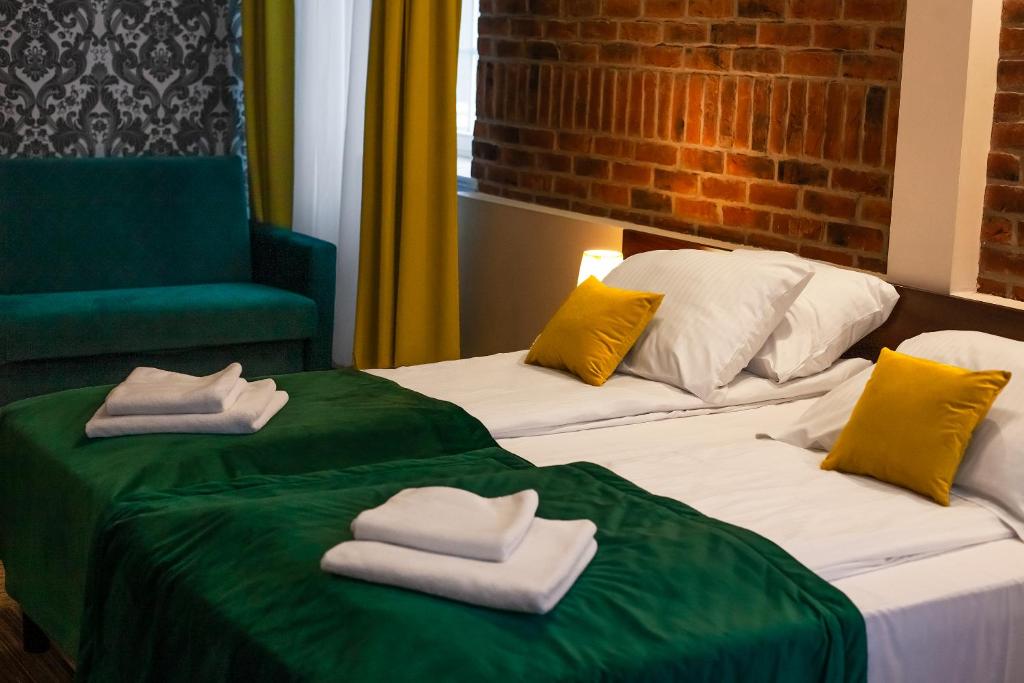 two beds with towels and a green chair at Hotel Artus - Old Town in Gdańsk