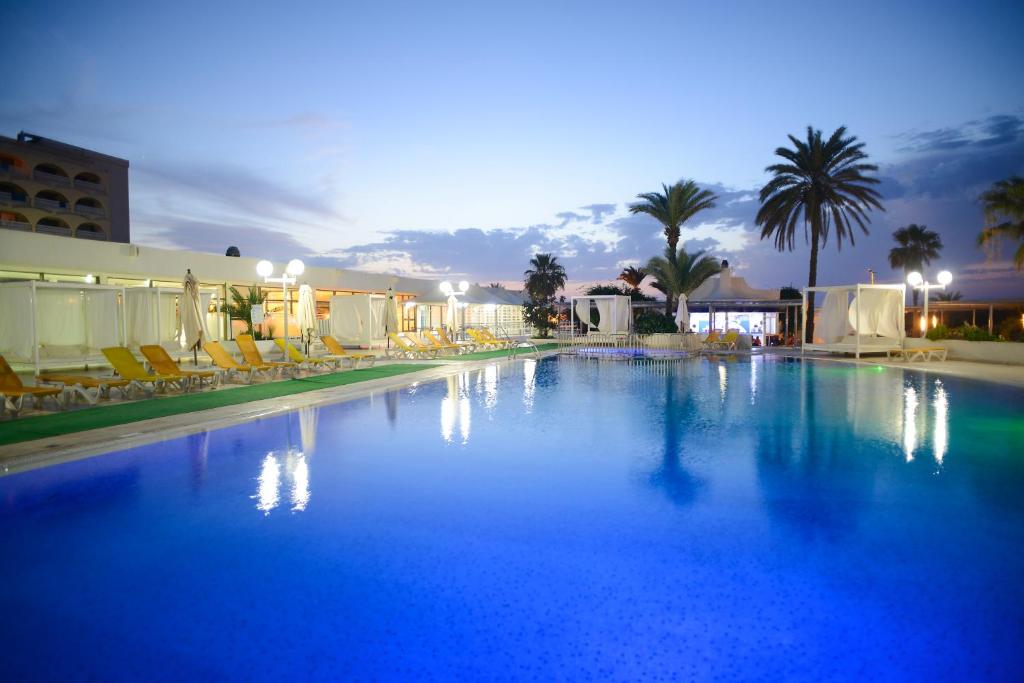 a large blue swimming pool with chairs and palm trees at One Resort Jockey Monastir in Monastir