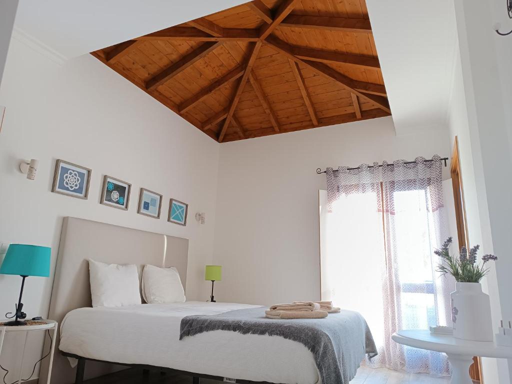 a white bedroom with a bed and a wooden ceiling at Casa do Alto in Tavira
