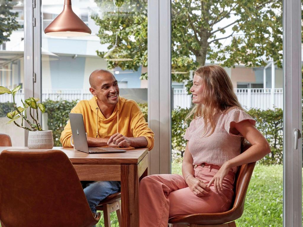 Ein Mann und eine Frau sitzen an einem Tisch mit einem Laptop in der Unterkunft Aparthotel Adagio Access Carrières Sous Poissy in Carrières-sous-Poissy