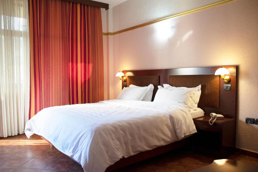 1 dormitorio con 1 cama grande con sábanas y almohadas blancas en Hotel Elysee, en Tirana