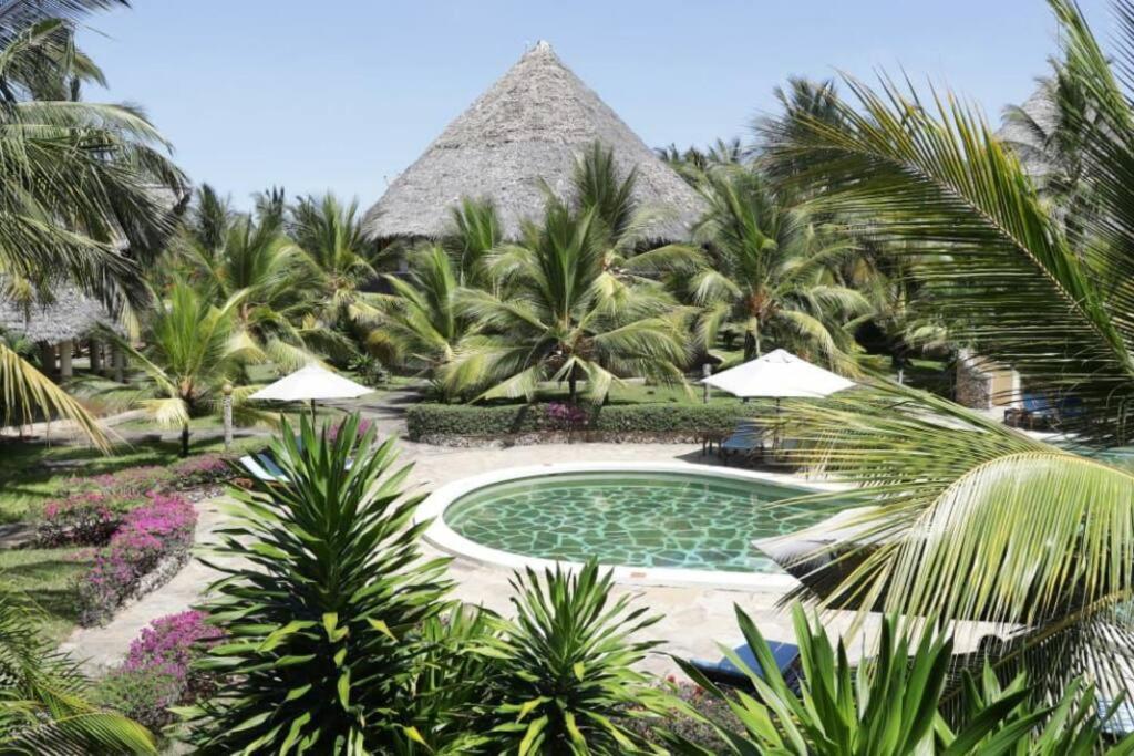 a resort with a swimming pool and palm trees at Tembo Beach Cottage in Malindi