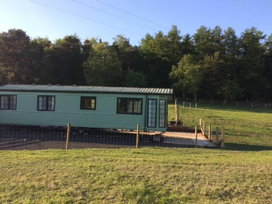 a green house in a field with a fence at Static Caravan (Cliburn Station) in Penrith