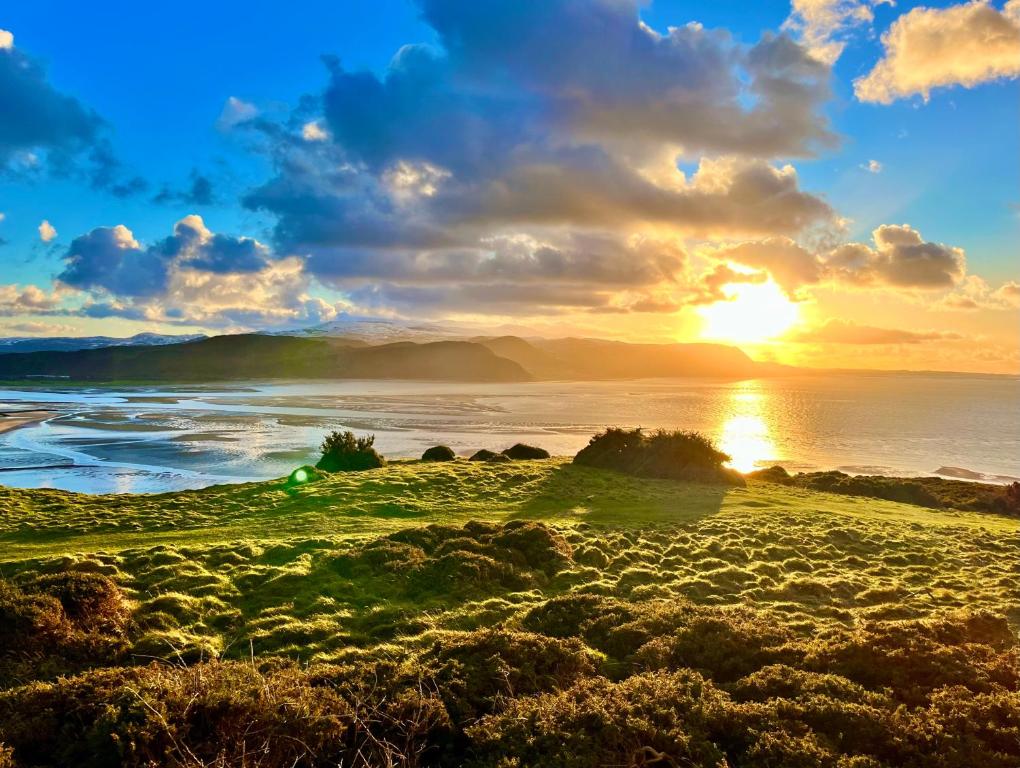 a sunset on the beach with the ocean and mountains at Llandudno Boutique style seaside retreat with stunning views in Llandrillo-yn-Rhôs