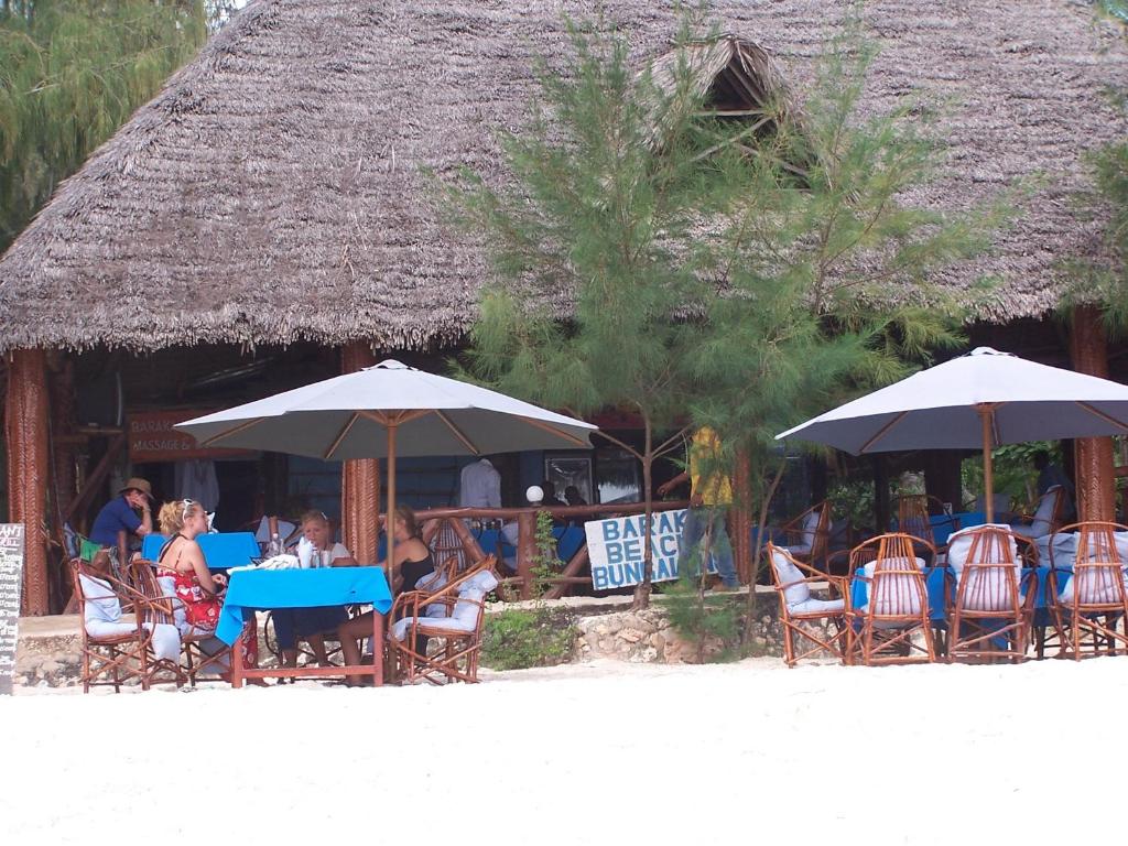 Un groupe de personnes assises à des tables sous des parasols dans l'établissement Baraka Beach Bungalows, à Nungwi