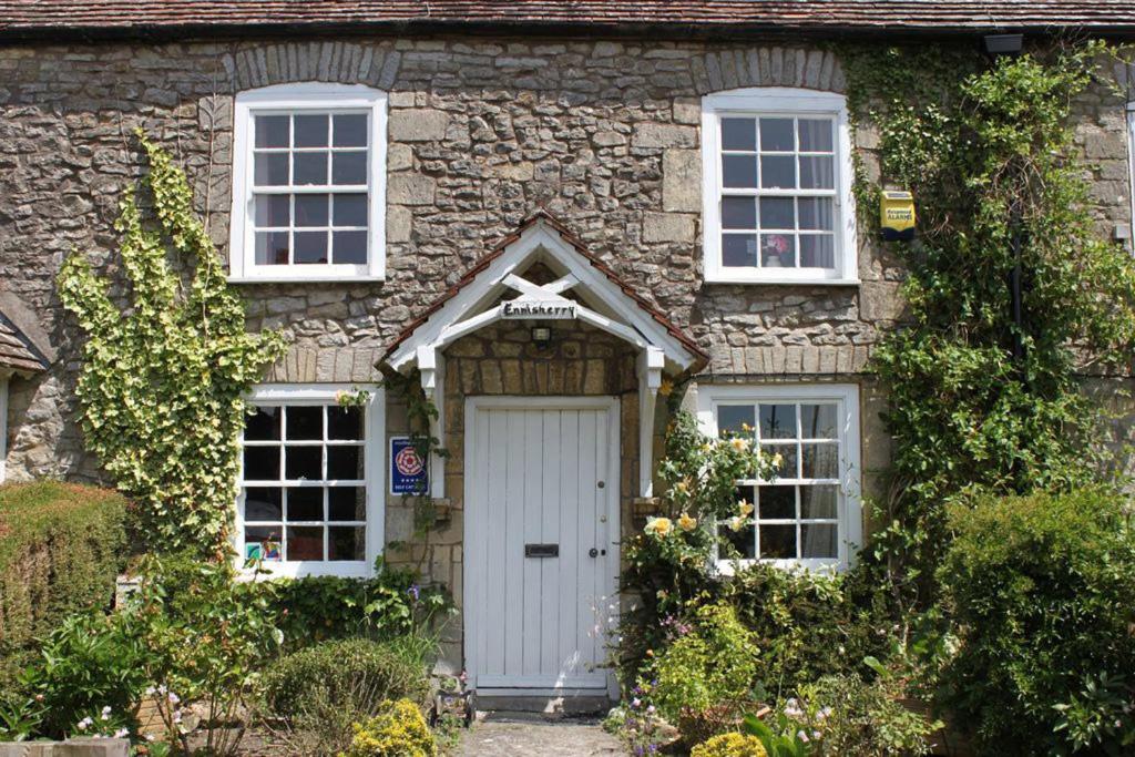 uma casa de pedra com uma porta branca e duas janelas em Enniskerry - The Loves Cottage em Shepton Mallet