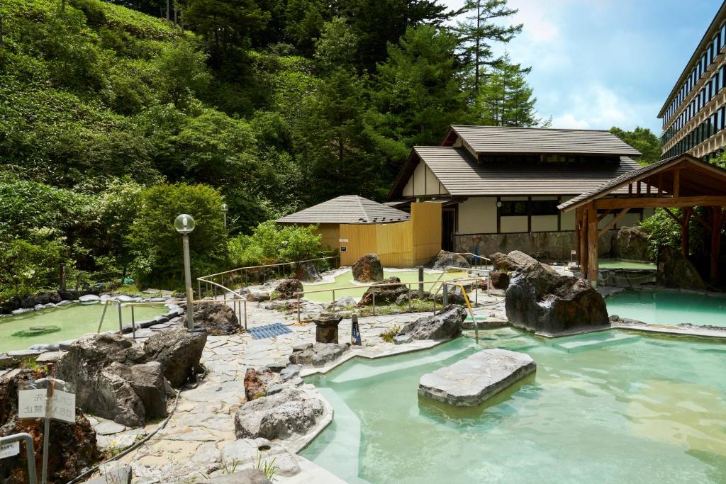 a pool of water with rocks and a house at Manza Kogen Hotel in Tsumagoi