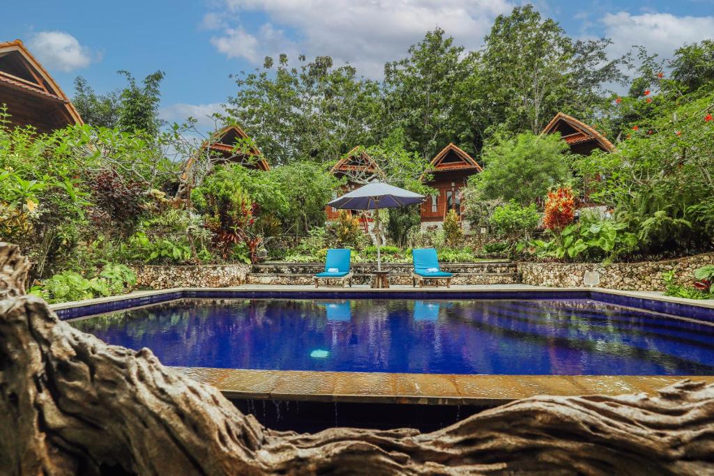 a pool at a resort with two chairs and an umbrella at The Tukad Gepuh Cottage and Resto in Nusa Penida