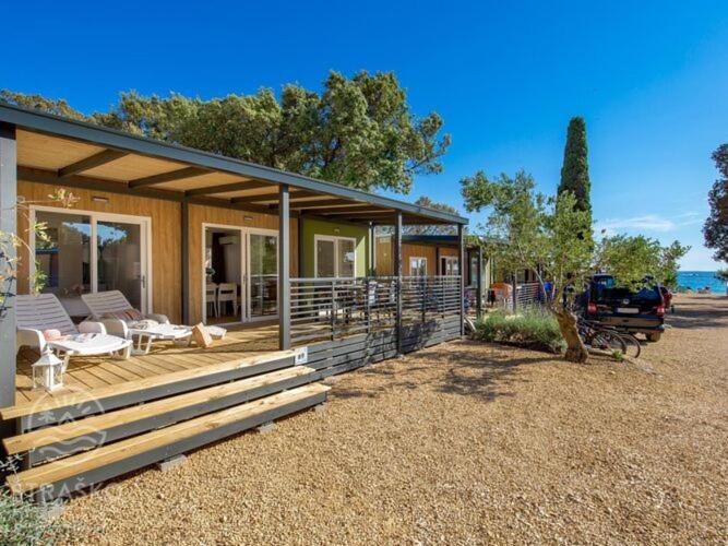 a house with a deck with a table and chairs at Mobile Home Pag near Pebble Beach & Pools in Novalja
