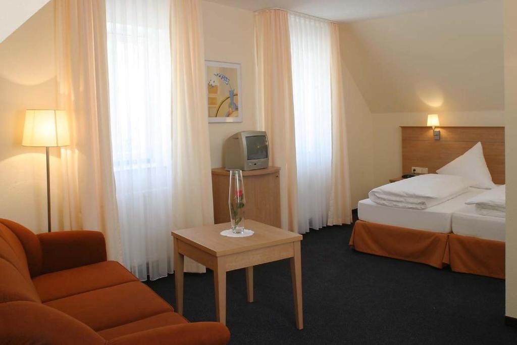 ラウダ・ケーニヒスホーフェンにあるGästehaus Zum Lammのベッド、椅子、テーブルが備わるホテルルームです。