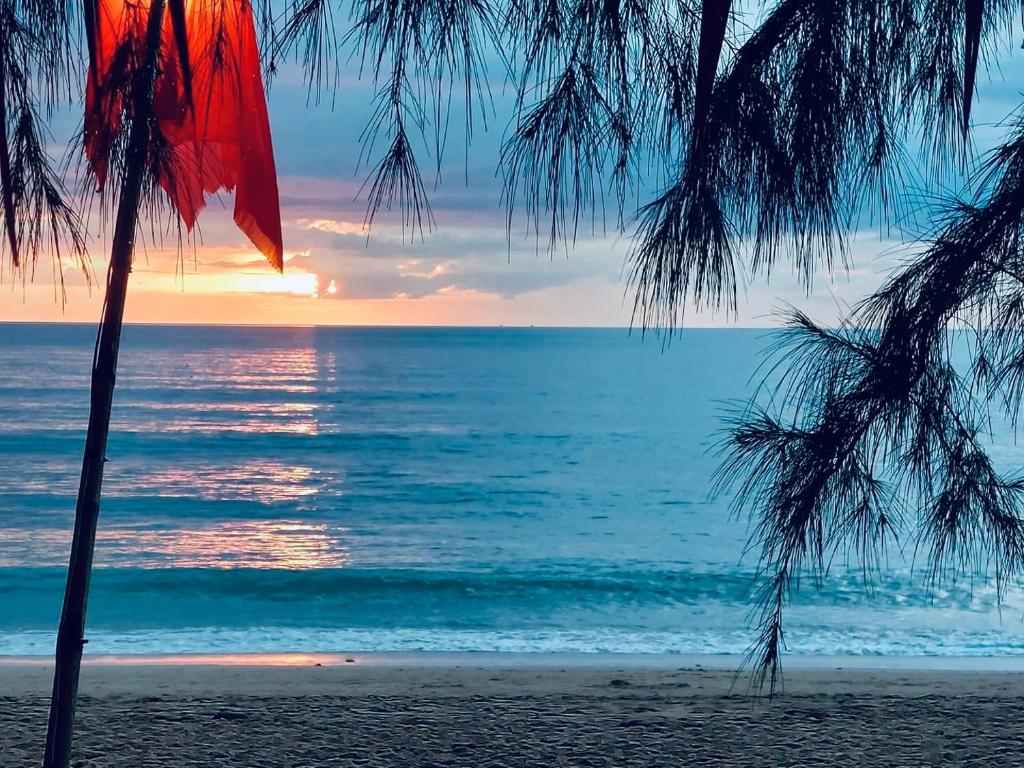 una puesta de sol sobre el océano a través de palmeras en una playa en Lanta L.D. Beach Bungalow, en Ko Lanta
