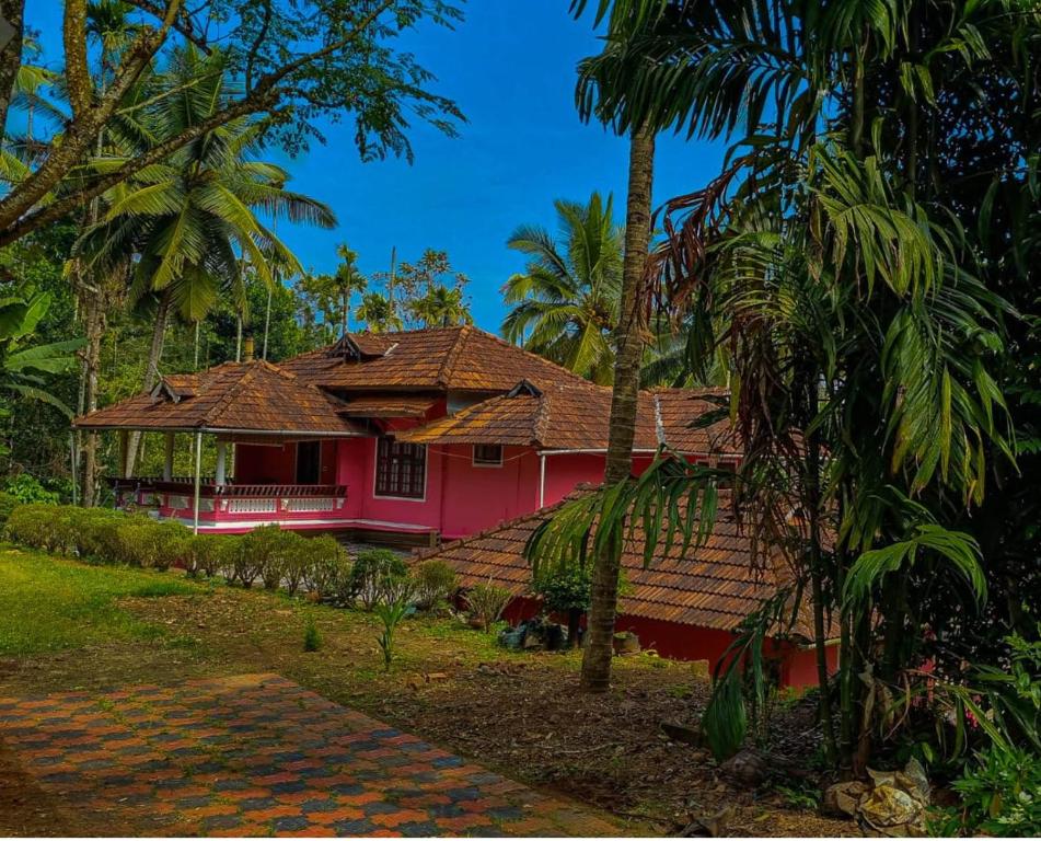 a pink house with palm trees in front of it at Spice Garden Farm house in Sultan Bathery