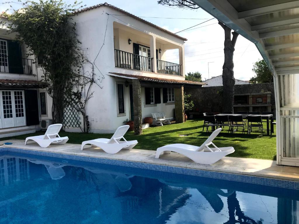 een zwembad met witte ligstoelen naast een huis bij Solar das Mimosas 2 casas in Sintra