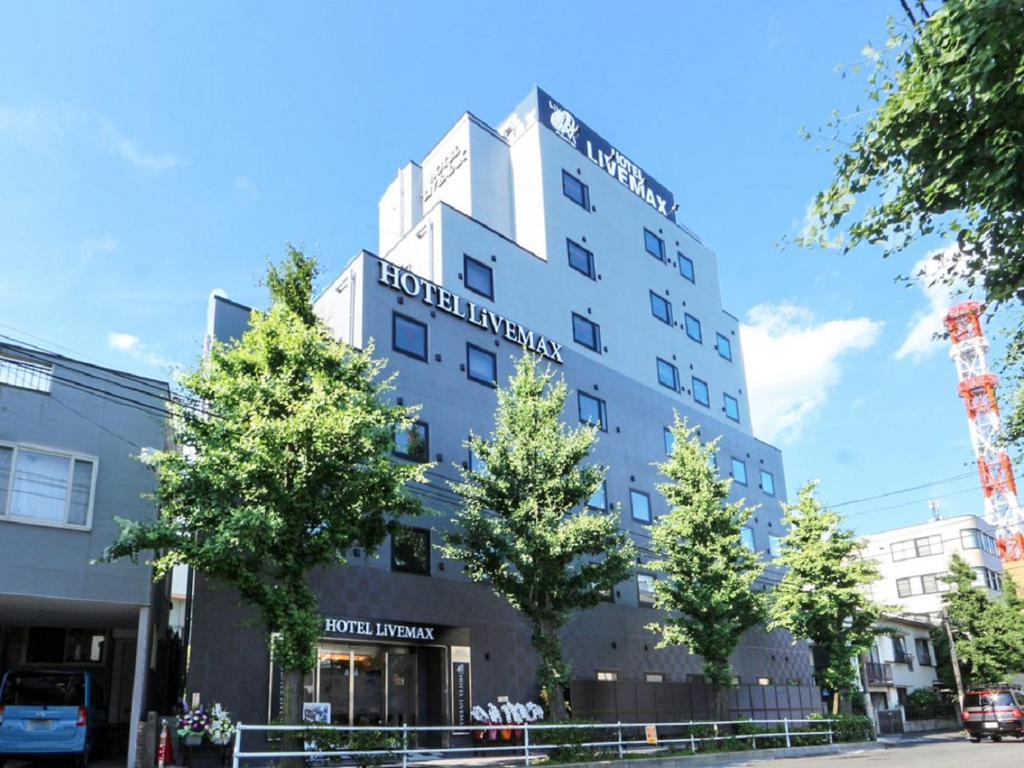 un edificio alto y blanco con árboles delante en HOTEL LiVEMAX Hachioji Ekimae, en Hachioji