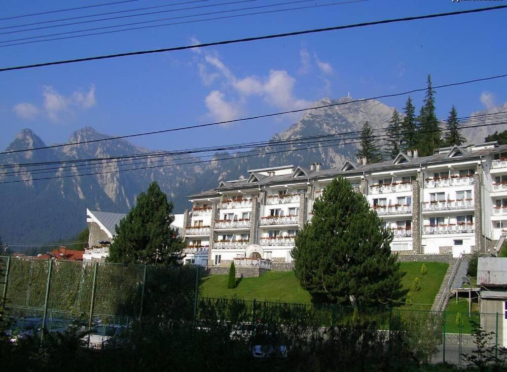a large white building with mountains in the background at Hotel Alexandros Busteni in Buşteni
