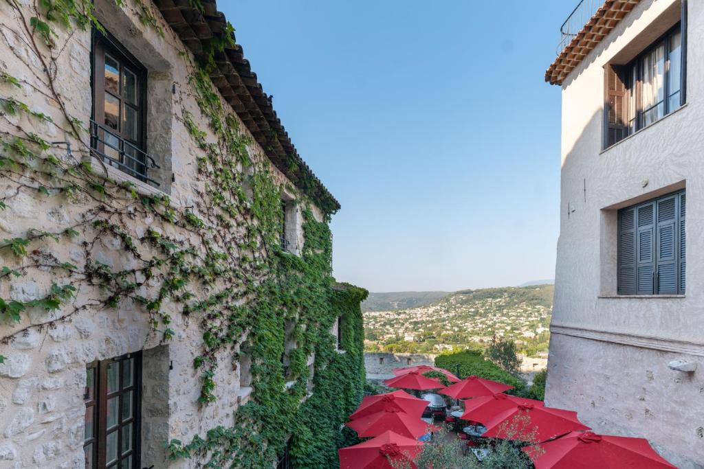 um edifício coberto de hera com guarda-chuvas vermelhos numa cidade em Hotel Le Saint Paul em Saint-Paul-de-Vence