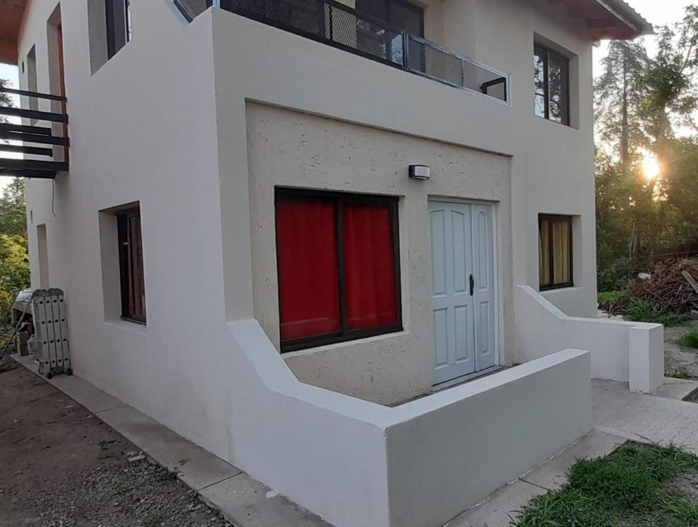 una casa blanca con una ventana roja en el lateral en COMPLEJO COMECHINGONES DPTO 3 2 HABITACIONES en Villa General Belgrano