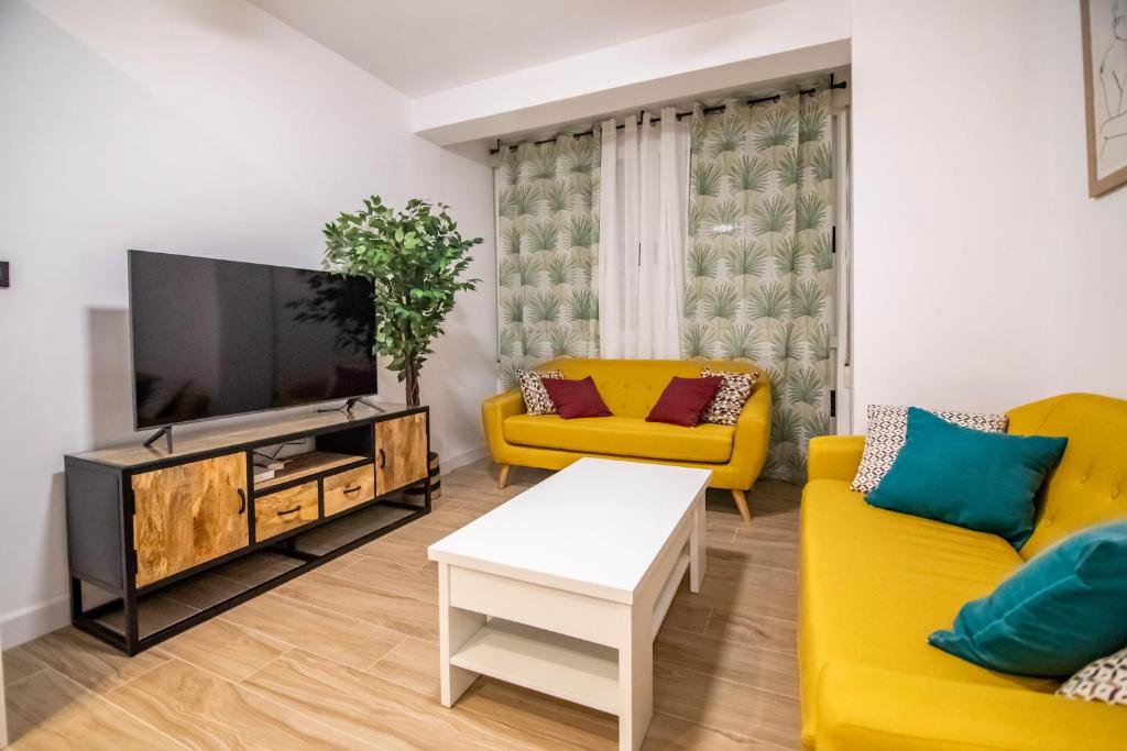 a living room with yellow furniture and a flat screen tv at tuGuest Avenida Madrid in Granada