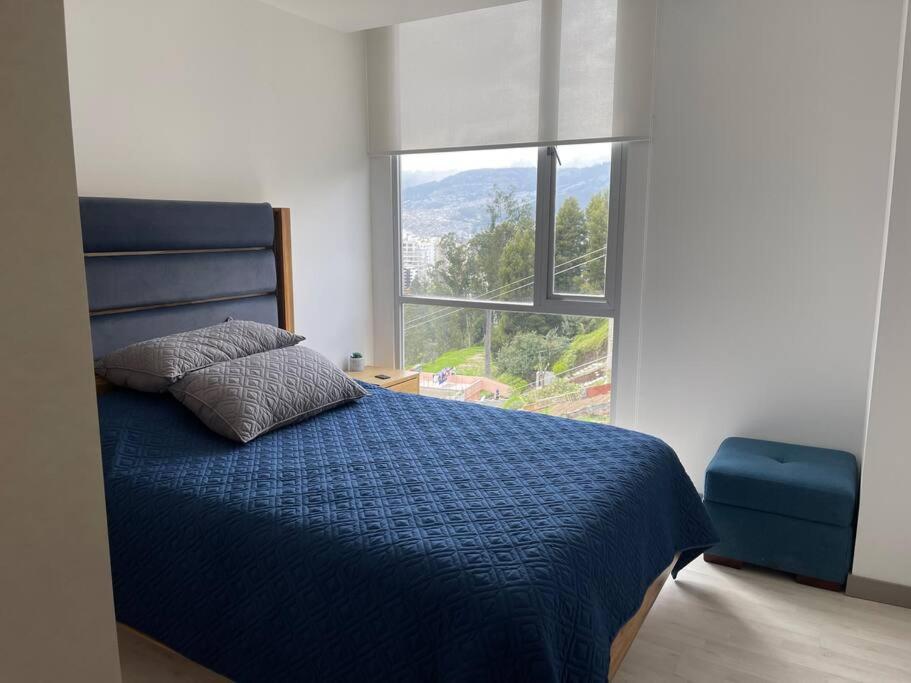 1 dormitorio con cama azul y ventana grande en Dpo 2 dorm(parqueadero wifi Netflix)vista pan. UIO, en Quito