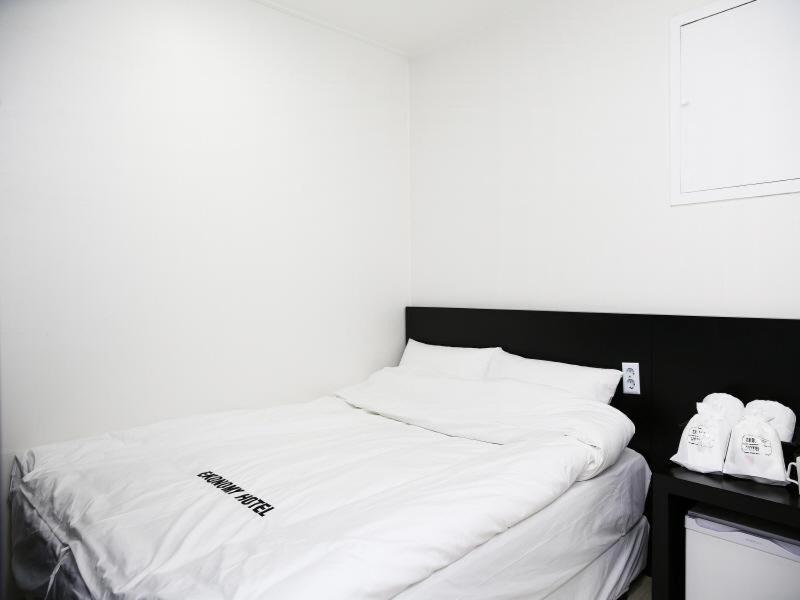 a bed with white sheets and shoes on a table at Korea guesthouse in Gumi