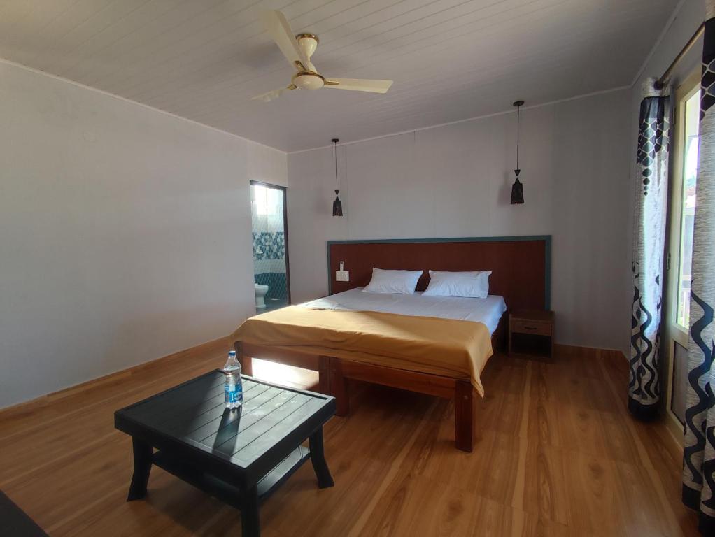 a bedroom with a bed and a table and a ceiling fan at Coral Beach Cottage in Māvalli