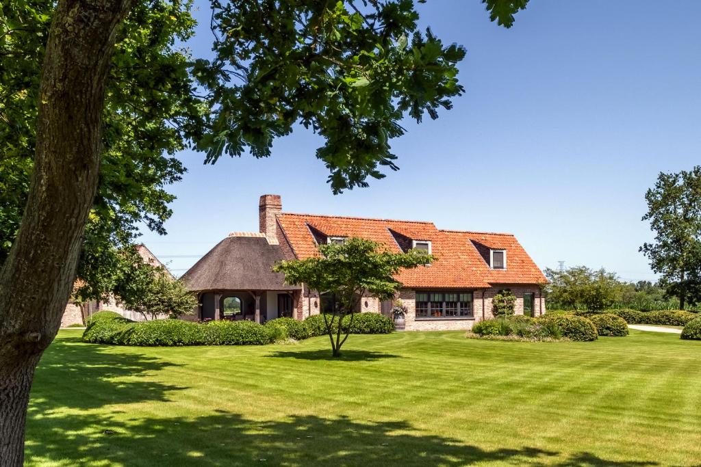 uma casa com um telhado laranja e um quintal verde em Hoeve den Akker - luxueuze vakantiewoningen met privétuinen en alpaca's nabij Brugge, Damme, Knokke, Sluis en Cadzand em Damme