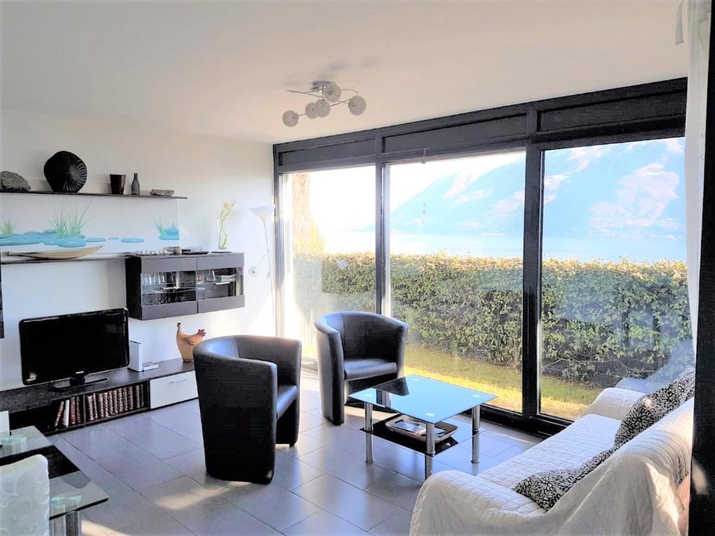 ein Wohnzimmer mit einem Sofa und Stühlen sowie einem großen Fenster in der Unterkunft Brissago: 3.5 Zi-Wohnung an extrem ruhiger Lage mit fantastischem Ausblick in Brissago